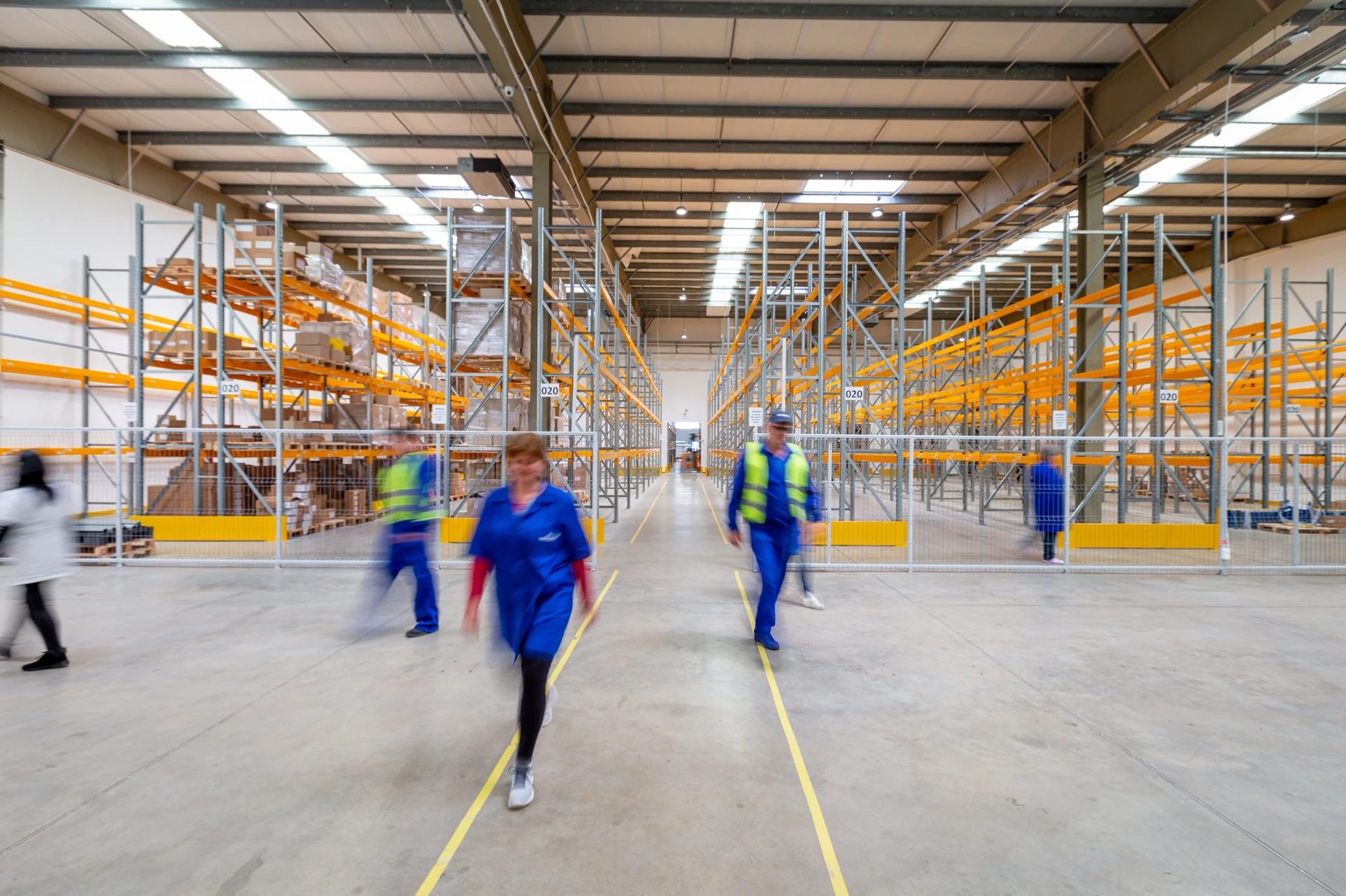 warehouse shelves, with three workers walking toward the camera